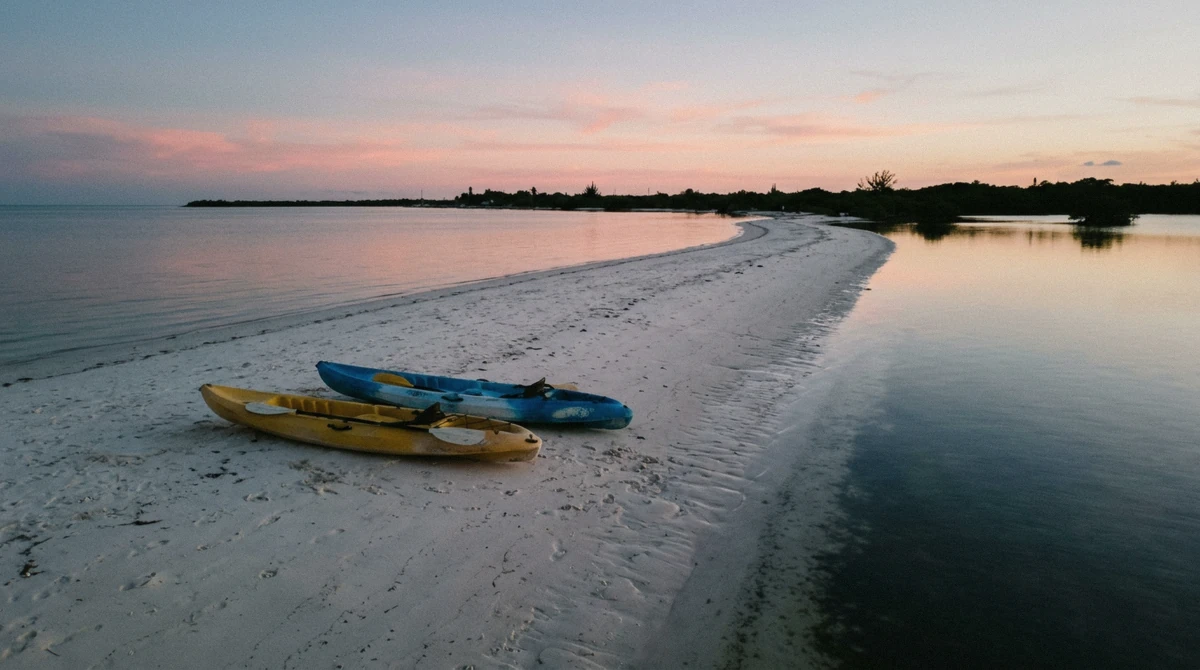 Two kayaks pulled up on a long white sandbar at dusk, flat calm water