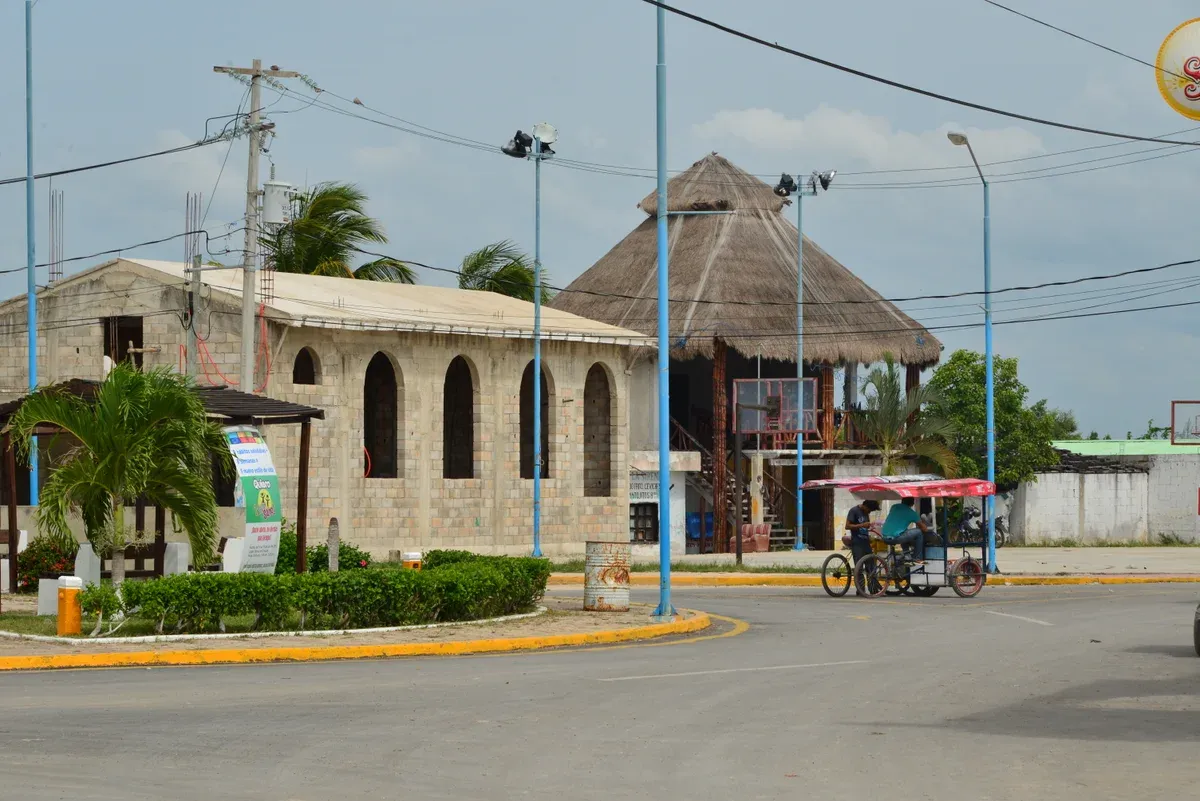 Stone building and thatched palapa beside a road and tricycle taxi at the Chiquilá waterfront