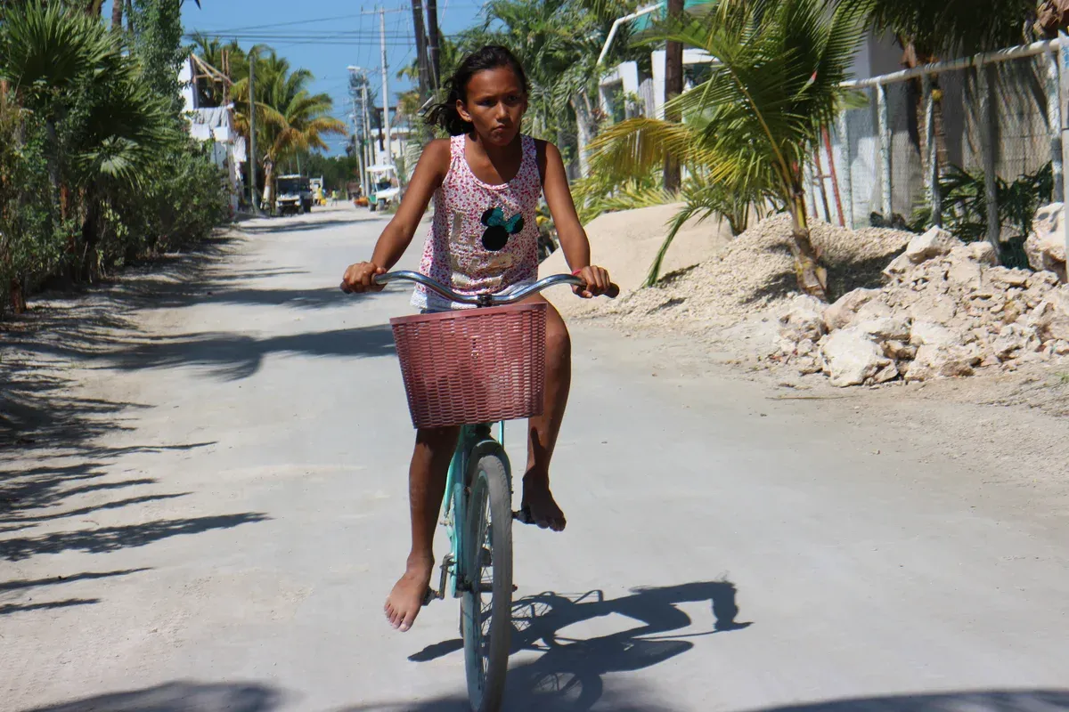 Girl cycling with a basket on a sandy street lined with palms in Holbox town
